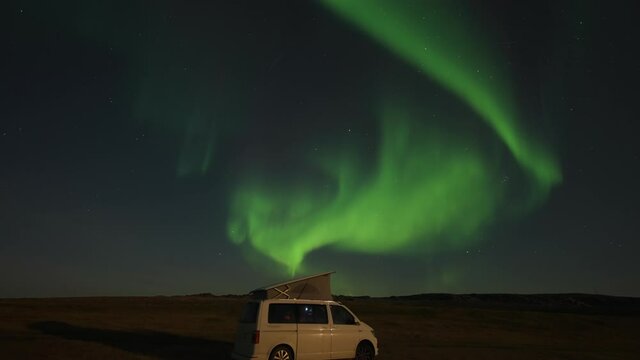 A stunning dance of the bright northern light in the starry night sky above the small white van with a popped-up tent