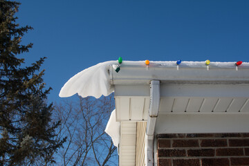 Holiday Christmas lights clipped to the gutter of a ranch style home; snow has covered them making...