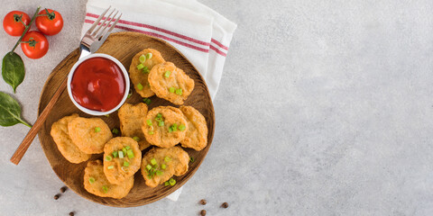 Golden chicken nuggets in a wooden plate, sprinkled with green onions and a lemon wedge. Copy space. Flatlay
