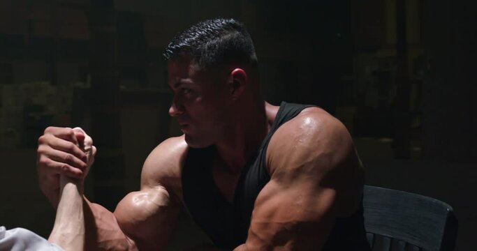 Camera circles a business man and a body builder as they battle in an arm wrestling match