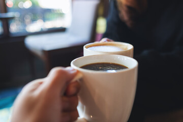 Closeup image of a couple people clinking coffee cups together in cafe
