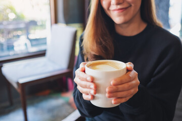 Closeup of a beautiful young woman holding and drinking hot coffee in cafe