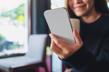 Closeup of a young woman holding and using mobile phone while drinking coffee in cafe