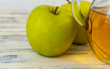 Green apples and jug with apple juice on wooden background