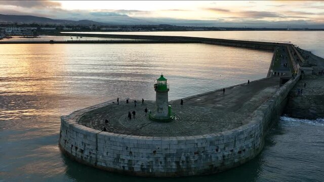 D&uacute;n Laoghaire Harbour, Dublin, Ireland. December 2021 Drone gradually orbits the West Pier lighthouse from the northeast with Monkstown and the Poolbeg Power Station in the distance at golden-hour.