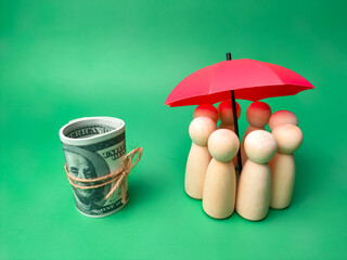 A group of wooden dolls are hiding under a red umbrella with banknotes,saving families, preventing risks and insurance concepts.