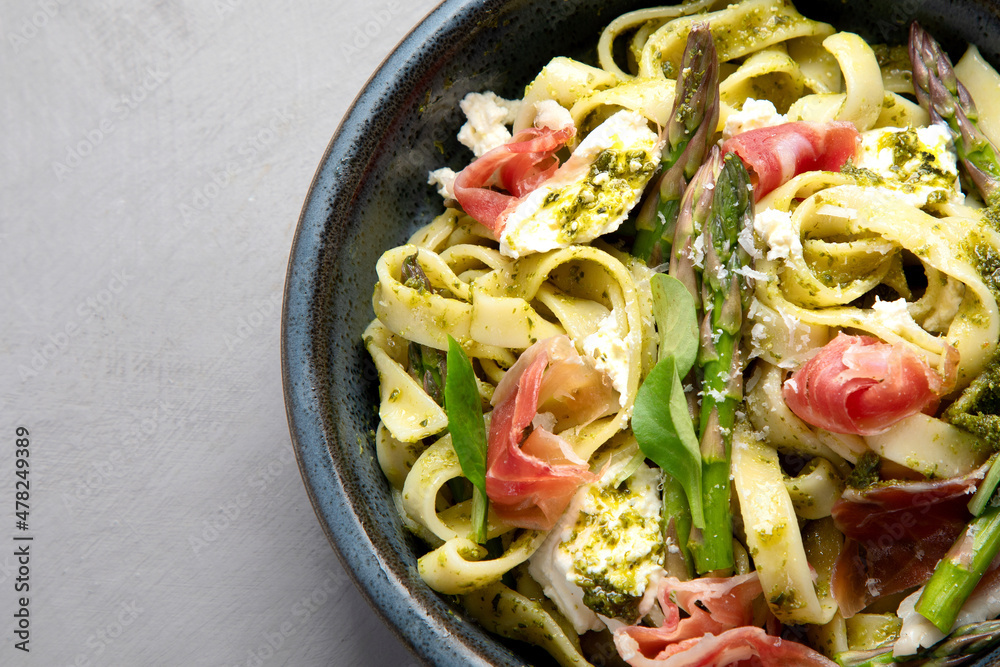 Wall mural pasta with asparagus and prosciutto on gray background.