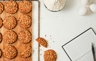 Homemade oatmeal cookies with flax and sesame seeds on a baking sheet, white background with copy space. Eggs, flour - ingredients for making cookies, table layout. Homemade holiday baked goods