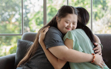 Close up shot of Asian happy lovely young chubby down syndrome autistic autism little daughter smiling hugging cuddling embracing showing warm love with mother sitting on cozy sofa in living room