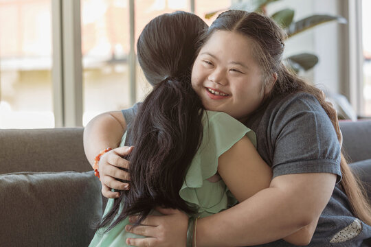 Close up shot of Asian happy lovely young chubby down syndrome autistic autism little daughter smiling hugging cuddling embracing showing warm love with mother sitting on cozy sofa in living room