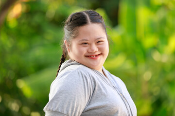 Portrait shot of Asian young chubby down syndrome autistic autism little cute schoolgirl with braid pigtail hairstyle model stand posing smiling look at camera in front blurred garden view background