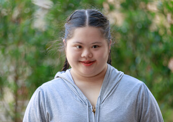 Portrait shot of Asian young chubby down syndrome autistic autism little cute schoolgirl with braid pigtail hairstyle model stand posing smiling look at camera in front blurred garden view background