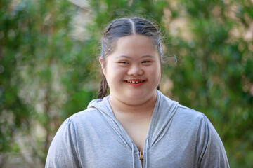 Portrait shot of Asian young chubby down syndrome autistic autism little cute schoolgirl with braid pigtail hairstyle model stand posing smiling look at camera in front blurred garden view background