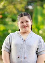 Portrait shot of Asian young chubby down syndrome autistic autism little cute schoolgirl with braid pigtail hairstyle model stand posing smiling look at camera in front blurred garden view background
