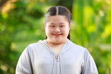 Portrait shot of Asian young chubby down syndrome autistic autism little cute schoolgirl with braid pigtail hairstyle model stand posing smiling look at camera in front blurred garden view background