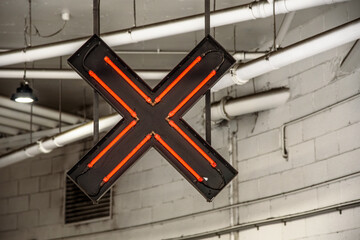 A red neon sign in the shape of an X to indicate the wrong way to enter a downtown parking lot