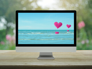Pink fabric heart love air balloon on tropical sea with desktop modern computer monitor screen on wooden table over blur flower and tree in park, Business internet dating online, Valentines day concep