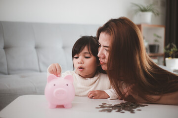 Mother and daughter putting coins into piggy bank. Family budget and savings concept. Junior...