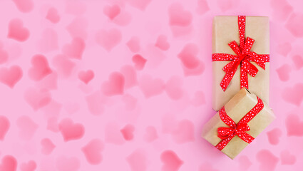 Wrapped craft paper boxes with gifts decorated with red bow on pink hearts background	
