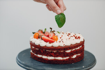 Pastry chef makes delicious red velvet cake. Cooking and decorating dessert with mint leaf.