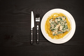 Portion of delicious meatballs with spinach in a creamy sauce and pasta on wooden background