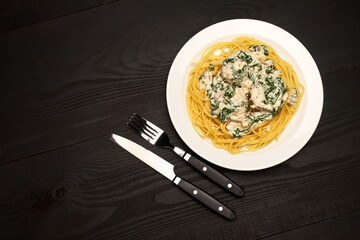 Portion of delicious meatballs with spinach in a creamy sauce and pasta on wooden background