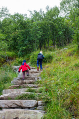 Children, toddler, brothers and father, climbing the stairs to Reinebringen, trekking path leading to the top of the mountain, where one can see Reine village and many fjords from above
