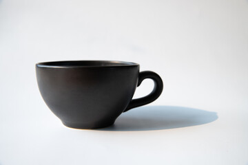 Matte black color coffee cup with natural sun light and black shade with isolated white background.