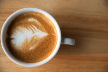 Closeup bird view of a cup of hot latte art coffee in white cup on wooden table background with natural sun light. Flat lay, top view style photo.