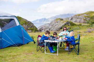 Happy family with three kids, wild camping in Norway summertime, people having breakfast adn coffee...