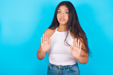 Young hispanic girl wearing tank top over blue background doing stop sing with palm of the hand....