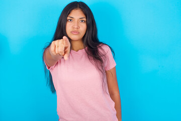 Cheerful Young hispanic girl wearing pink T-shirt over blue background indicates happily at you, chooses to compete, has positive expression, makes choice.