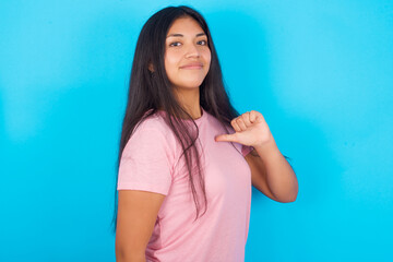 Closeup of cheerful Young hispanic girl wearing pink T-shirt over blue background looks joyful,...