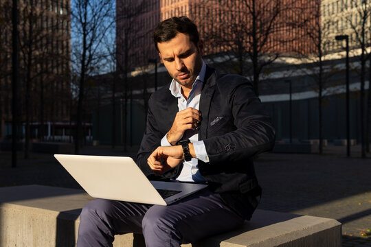 Serious businessman checking time while working on laptop on street