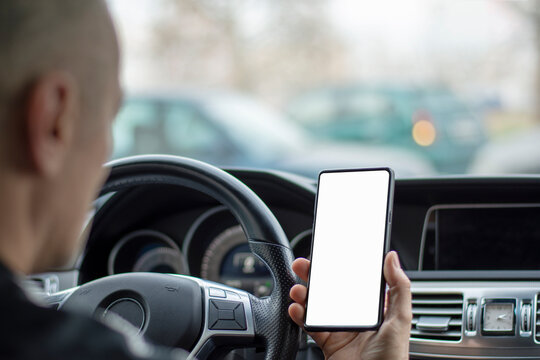 Mockup image of a man holding and using mobile phone with blank screen while driving car