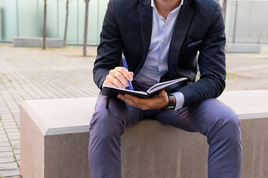 Unrecognizable businessman writing in notebook on street