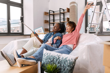 moving, people and real estate concept - happy smiling women with smartphone and selfie stick...