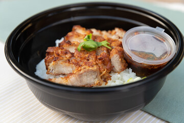 Closeup of food as Crispy fried pork belly with Thai spicy sauce, cucumber on white jasmine rice in black modern bowl on clean cream and green minimal clolor table cloth background and texture.