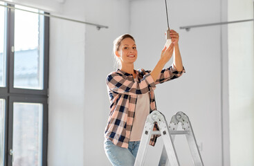moving, electricity and repair concept - woman changing light bulb at new home