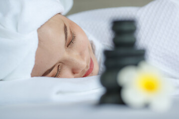 Obraz na płótnie Canvas Close up shot white yellow plumeria flower bloom with oil and hot stones compress stuff in towel placing on massage bed while spa therapy Asian female client lay down relaxing in blurred background