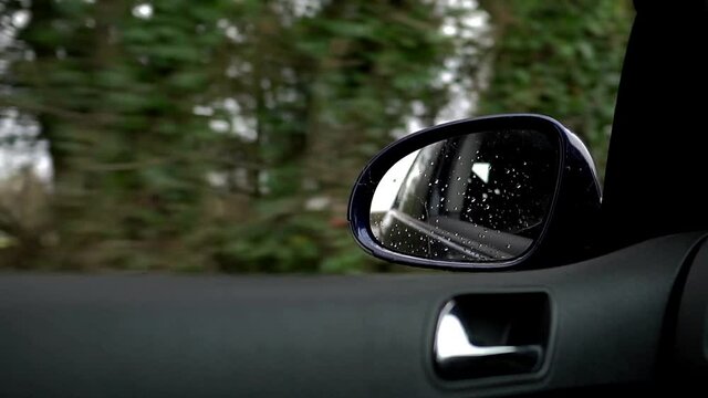 Slow motion footage from inside a VW Golf car looking out of the window as the car drives through the countryside. Wing mirror in right side of frame and door in lower section. Slow motion car video