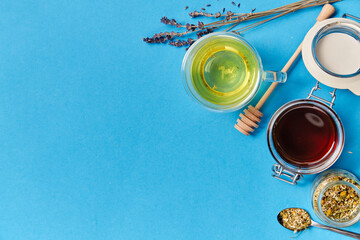 herbal medicine and health concept - close up of cup of chamomile tea, honey in glass jar with dipper and dry lavender flowers on blue background