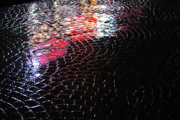 Colorful reflections on wet dark cobblestone street.  Rainy evening. Horizontal photo with copy...