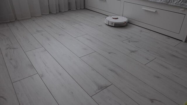 Modern robot vacuum cleaner vacuums the light floor in the bedroom. A smart wireless vacuum cleaner cleans the laminate from dust. Modern automated smart home devices that simplify life.