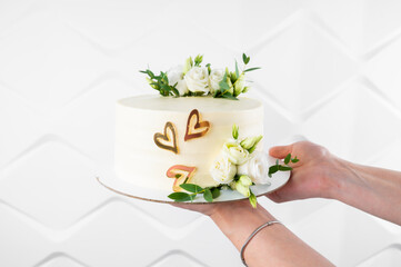 Pastry chef holding tasty wedding cake with floral decoration on white background, close up