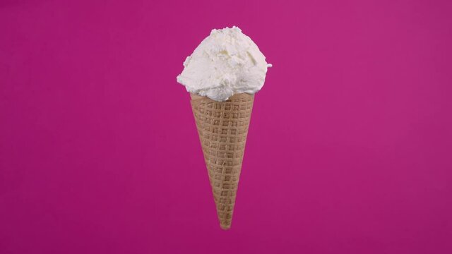 Tasty vanilla ice cream in waffle cone. Sweet dessert, rotating soft cream, gelato icecream scoop over pink background