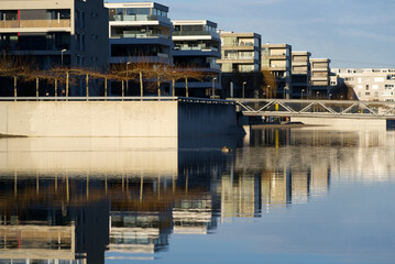 Apartment buildings at border of pond at public park with bridge in the background on a sunny winter day. Photo taken December 31st, 2021, Zurich, Switzerland.