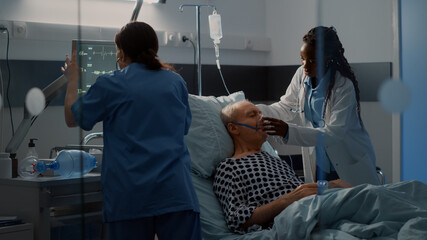Patient with breathing problems in hospital ward bed needing reanimation help from nurse and african american doctor using oxygen tube. Old man with disease in intensive care room
