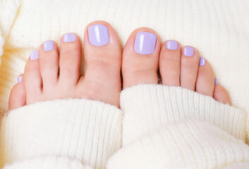 Female feet with purple pedicure on white knitted surface, top view.
