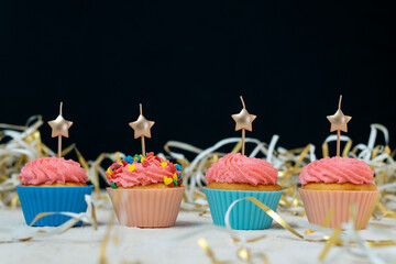 Birthday cupcake with candles in the form of stars in festive tinsel on black background. Space for text.
